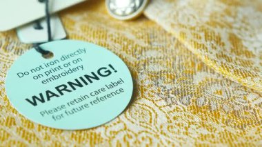 Doğrudan ütülemeye karşı tavsiye veren nakışlı bir kumaş bakım etiketinin yakın çekimi.