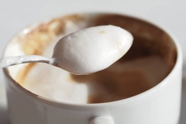 Bol köpüklü bir kaşık masanın üzerinde sıcak bir kahve fincanı üzerinde süzülür..