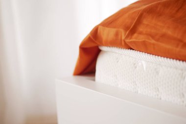 Üzerinde turuncu bir battaniye olan beyaz bir yatağın yakın çekim görüntüsü..