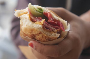 Bir insan et ve sebzelerle dolu canlı bir sandviçin tadını çıkarır..