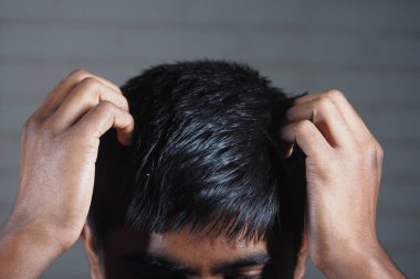 Genç bir adam stresli görünüyor, saçlarını iki eliyle kapalı tutuyor..