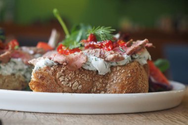 Açık sandviçte taze biftek, otlar ve ekmek üzerine renkli malzemeler yer alıyor..