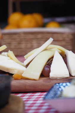 Tahtada çeşitli peynir dilimleri ve yakınlarda taze meyve..