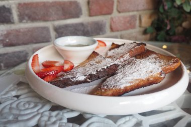 Pudra şekeri ve çilekle süslenmiş bir tabak Fransız tostu..