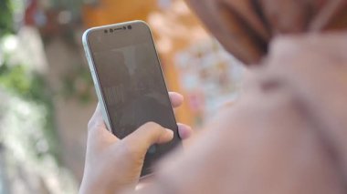 Bir kadın dışarıda güneşli bir günün tadını çıkarırken akıllı telefonuyla meşgul olur..