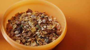 Besleyici bir kase granola canlı turuncu bir yüzeye oturur..