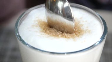 Bir kişi kafe masasındaki kremalı içeceğe esmer şeker ekler..