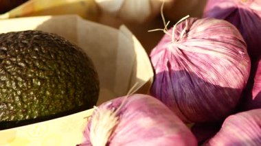 Canlı mor sarımsak ve olgun avokadolar bir pazarda sergileniyor..