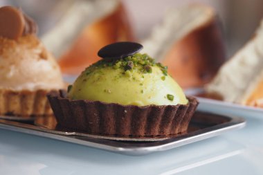 Canlı yeşil bir tatlı tepside zarif bir şekilde oturur. Etrafı hamur işleriyle çevrilidir..