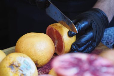 Eller, turunçgillerle çevrili ahşap bir tahtanın üzerinde canlı bir greyfurt dilimler..