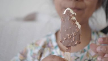 Bir çocuk elinde çikolata kaplı bir dondurmayla gülümsüyor..