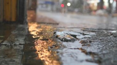 Şiddetli yağmurlar su birikintilerinin oluşmasına yol açar, şehir ışıklarını ve renklerini yansıtır.