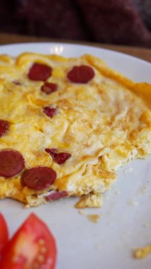 Lezzetli bir peynir ve sosisli omlet taze domates dilimleriyle yenir..