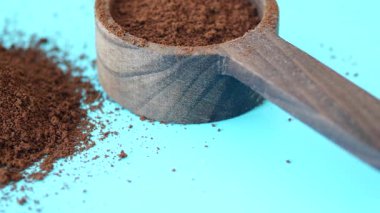 Canlı mavi bir fon üzerinde ahşap bir kepçenin içinde taze öğütülmüş kahve sergileniyor..