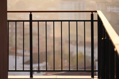 Gün batımının ışığı, uzak binalarla dolu bir balkon korkuluğuna sıcak bir ışık saçıyor..