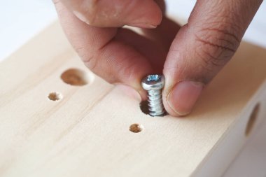 Bir insan, metal vidayı dikkatle tahta bir parçaya yerleştirir..