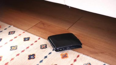 Kanepenin altındaki ahşap zeminde sıcak bir yerde siyah bir cüzdan duruyor..