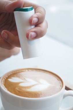 Kahve fincanına Latte sanatıyla tatlandırıcı serpiştiren ellerin yakın çekimi, 