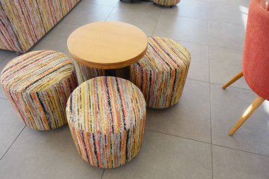 Canlı bir kafede küçük ahşap bir masanın etrafında renkli tabureler..