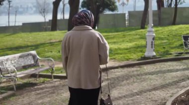 Güneşli bir günde başörtüsü takmış genç bir kadın parkta yürüyor..
