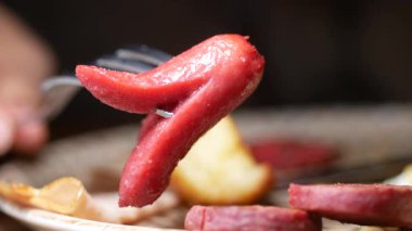 Yemek sırasında çatalla lezzetli sosisler yiyen biri..