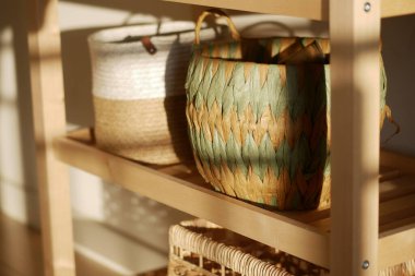 Ahşap bir rafta düzgünce dizilmiş renkli el yapımı sepetler..