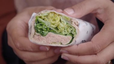 Bir insan taze sebze ve protein katmanlarıyla dolu sağlıklı bir sargı tutar..