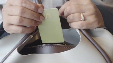 Sıradan bir ortamda kart çekmek için el çantasına uzanır..