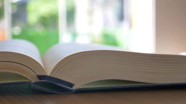 Bir insan, pencerenin yanındaki masada açık bir kitapla rahatlar..