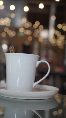 Sıcak bir kafe atmosferinde beyaz bir fincan bir tabağın üzerinde oturuyor..