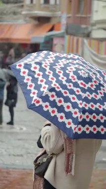 Yağmurlu bir günde bireyler renkli bir şemsiye altında dururlar.