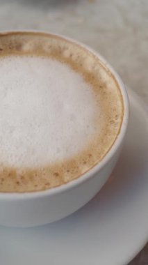 Kafede köpüklü sütle kaplı sıcak bir bardak kapuçino bekliyor..