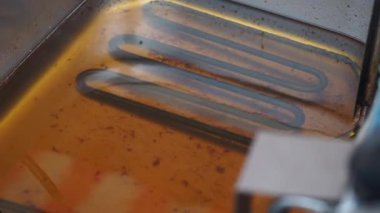 Kızartma yağına batırılmış ısıtma elementinin yakın görüntüsü, aşınmayı gösteriyor..