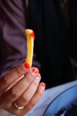 Canlı ojeli bir el ketçapla kaplı tek bir patates kızartması tutar..