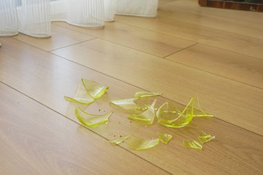 Ahşap zeminde yeşil cam bir nesnenin parçaları kırılmış..