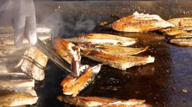 Şef güneşin altında açık hava pazarında lezzetli ızgara balıklar hazırlar..