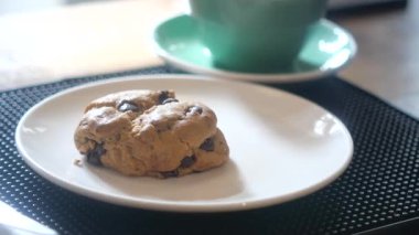 Lezzetli bir kurabiye bir tabakta, bir kafede sıcak bir içeceğin yanında oturur..