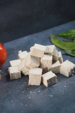 Taze tofu küpleri bir domates ve yeşil yaprakların yanında düzenlenir..