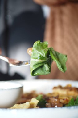 Sıradan bir yemek ortamında çatal dolusu taze yeşilliğin tadını çıkaran bir insan..