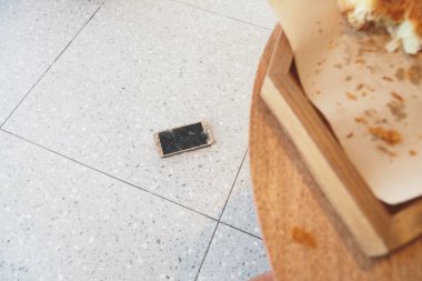 Ahşap bir masanın yanında yerde yatan kırık bir akıllı telefon. .