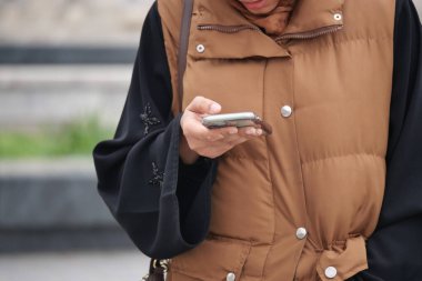 Bir insan parkta sıradan bir yelek giyerken akıllı telefonunu kontrol eder..