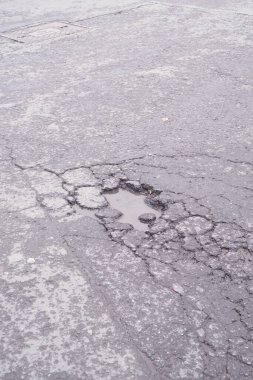 Çatlamış bir caddede, gri gökyüzünün altındaki çukurda yağmur suyu birikintileri.