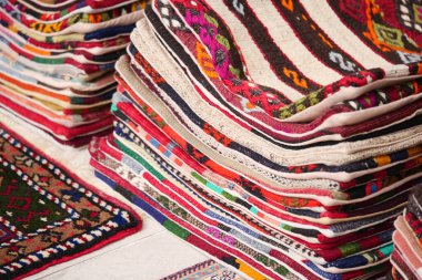 Gündüz yoğun bir pazarda istiflenmiş çeşitli renklerde el yapımı halılar.