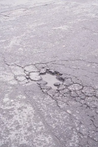 Çatlamış bir caddede, gri gökyüzünün altındaki çukurda yağmur suyu birikintileri.