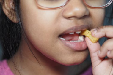 Genç bir kız atıştırmalık bir şeyler ısırır, yemek yerken odaklanır ve zevk alır..