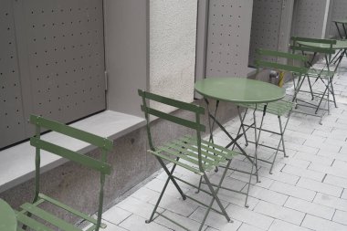 Küçük yeşil masalar ve sandalyeler açık alanda sakin bir avlu oluşturur..