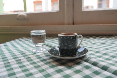Süslü bir bardakta bir bardak suyun yanında servis edilen Türk kahvesi..