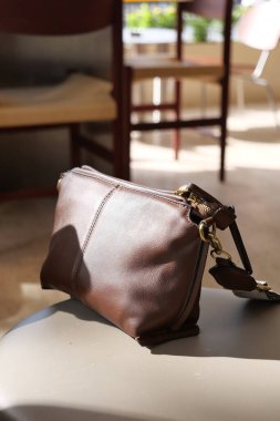 Kahverengi deri bir çanta güneşli bir kafede bir masanın üzerinde duruyor..