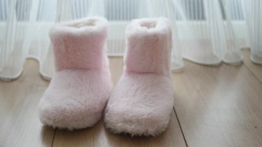 Yumuşak pembe terlikler bir perdenin yanındaki ahşap zemine konur..