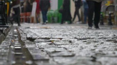 Kalabalık bir cadde bulutlu gökyüzünün altında yürüyen insanlarla dolu..